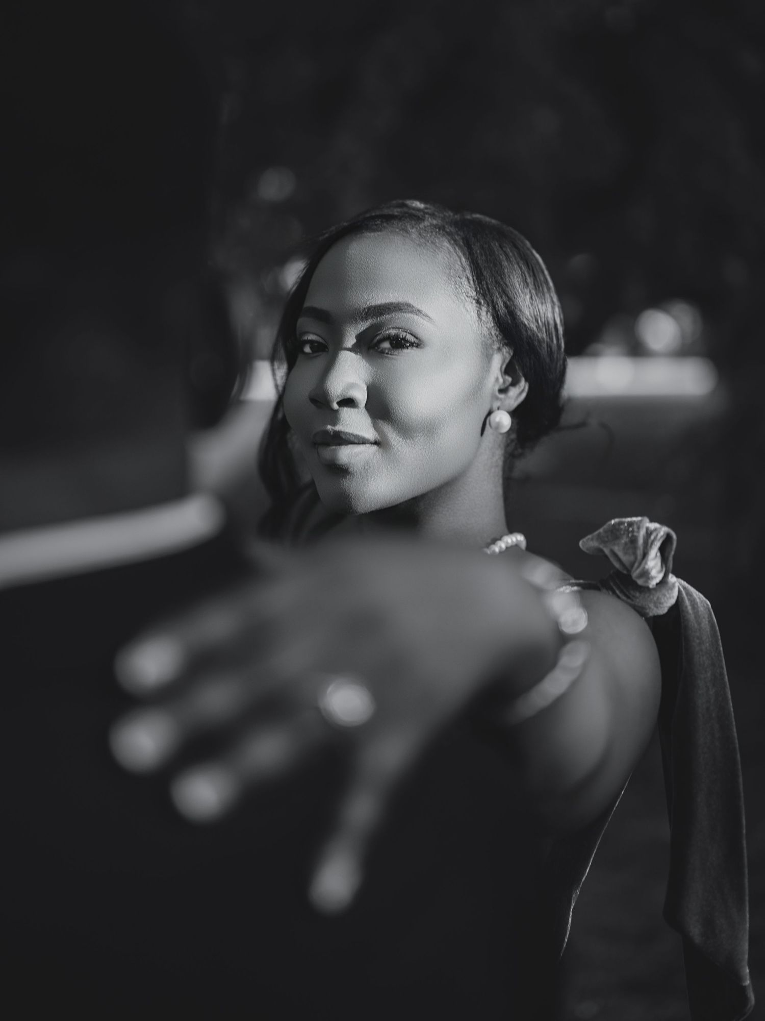 Black and white portrait of a beautiful Black woman reaching toward the camera in an outdoor setting.