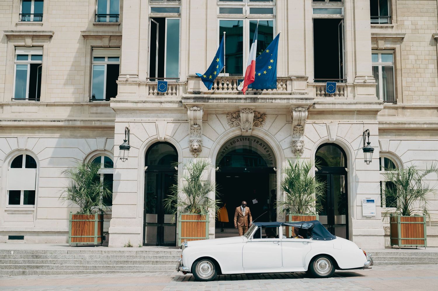 Elegant white vintage convertible car parked before a European building with French flags.