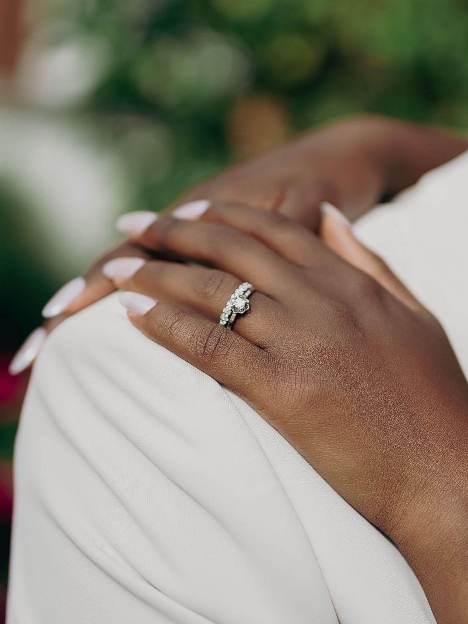 Close-up of diamond wedding ring set on bride's hand with white manicured nails.