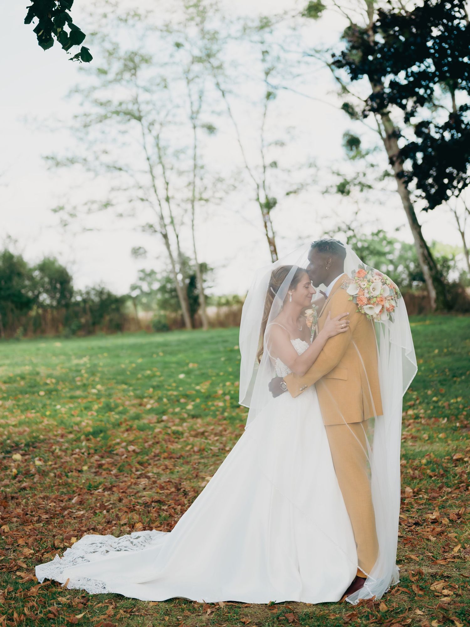 Bride and groom sharing romantic moment under bridal veil in lush outdoor garden setting.