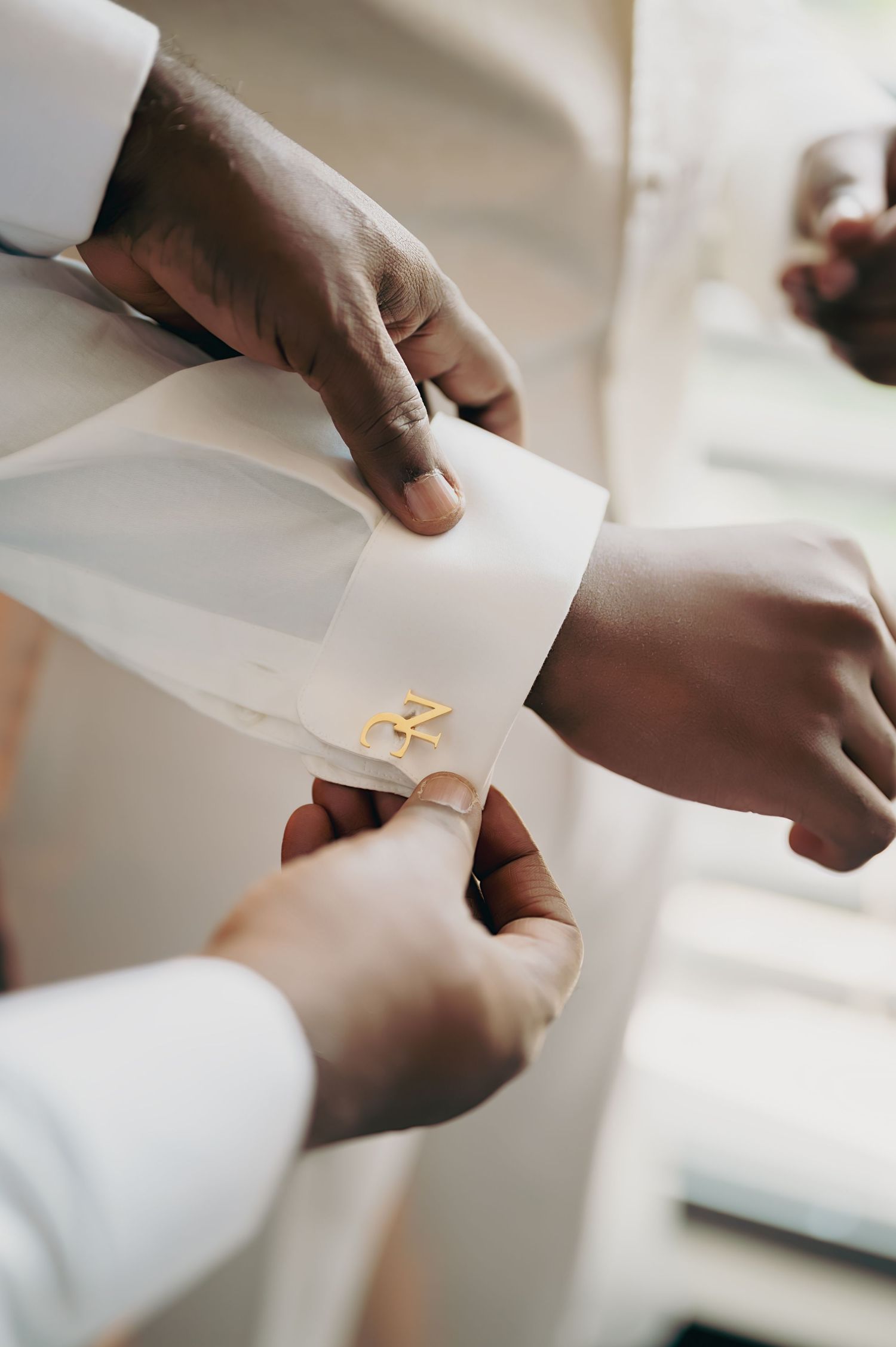 Close-up of golden monogram cufflinks being fastened on a white dress shirt sleeve.
