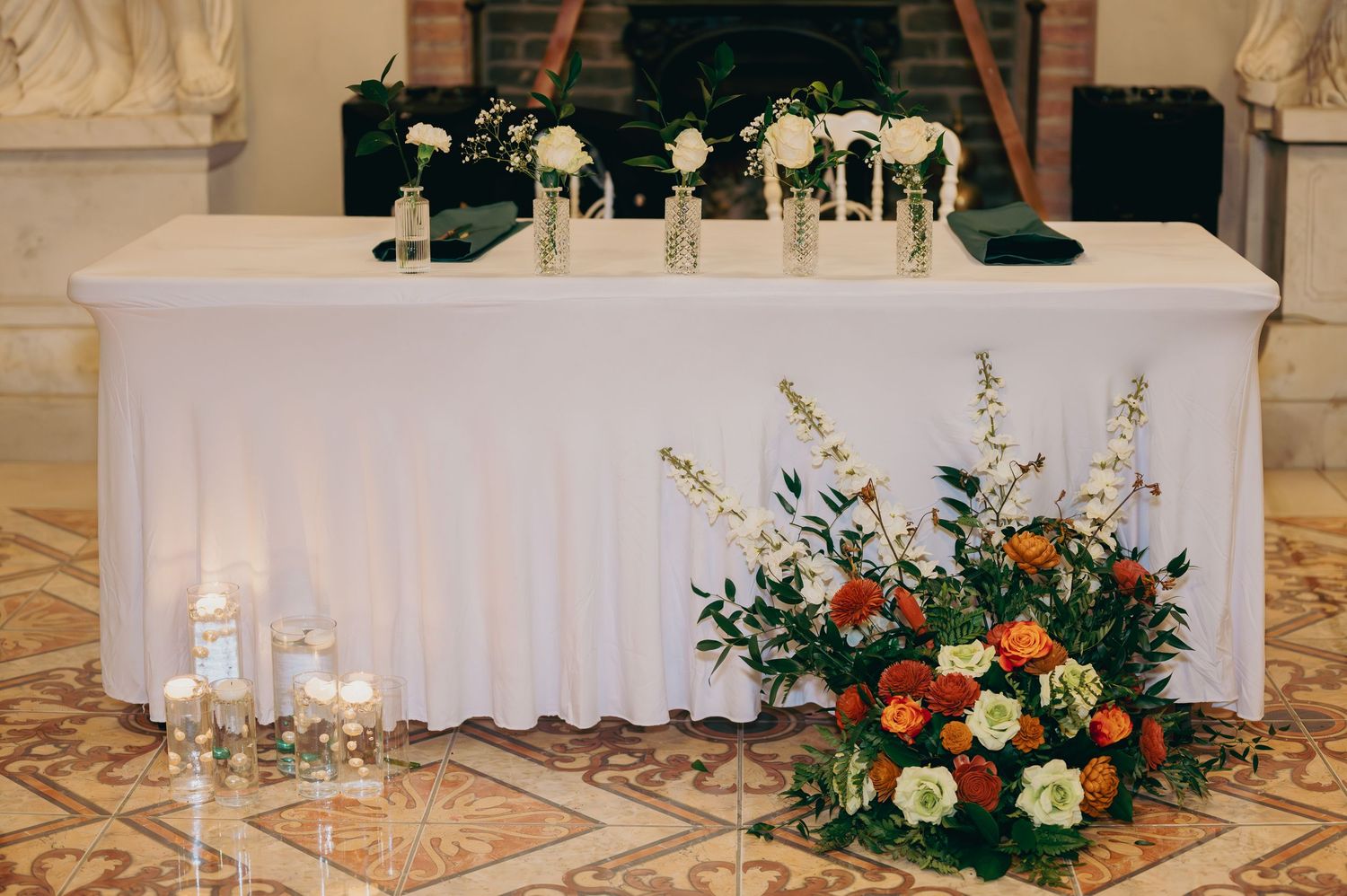 Elegant wedding sweetheart table with white floral arrangements and colorful flower display on marble floor.