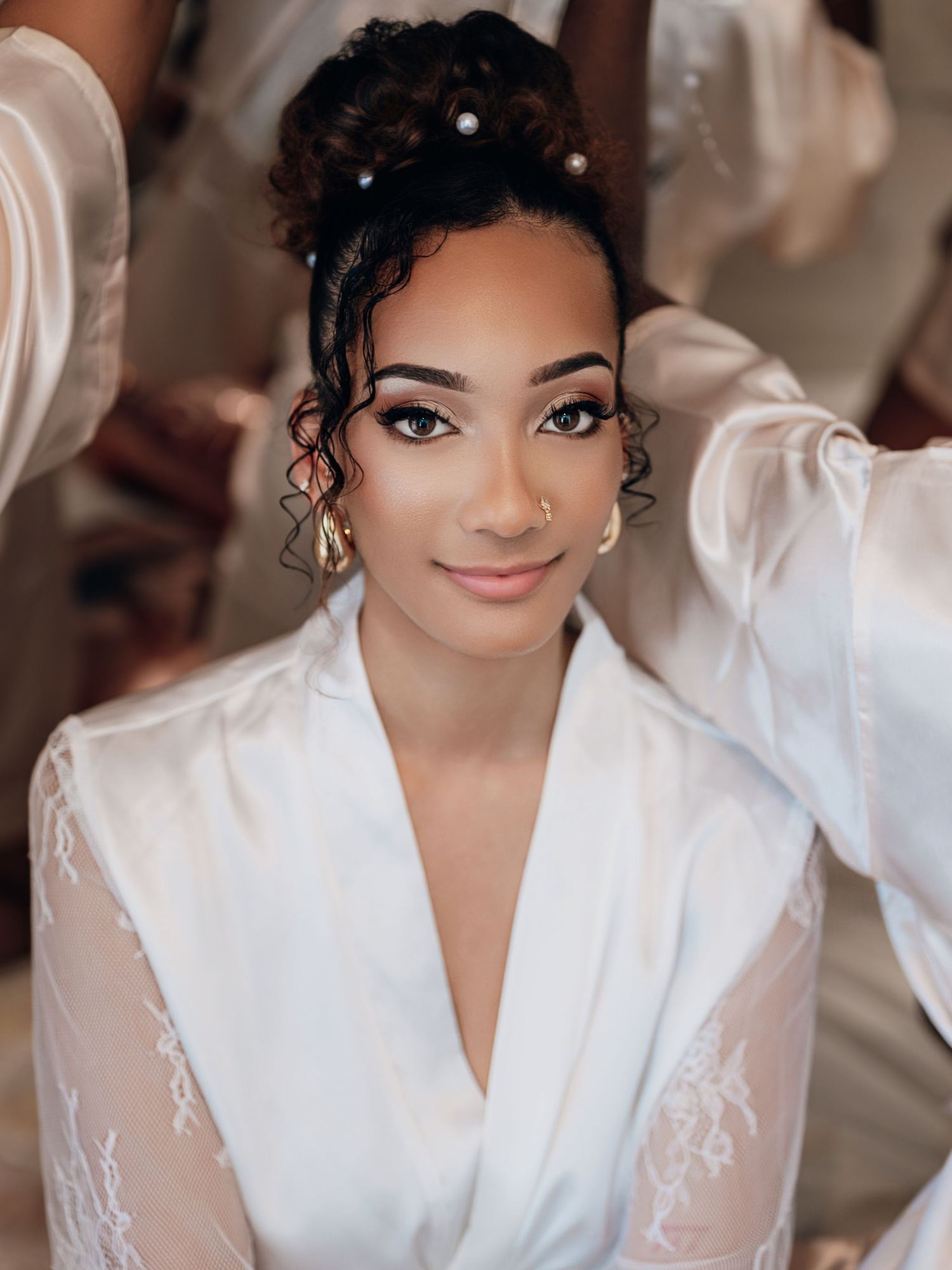 Beautiful bride with pearl hair pins and gold earrings wearing a white lace robe on her wedding day.