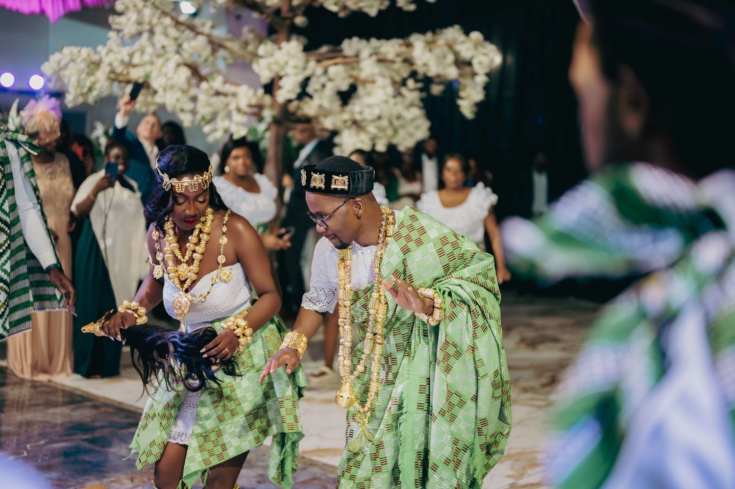 Guests in vibrant green traditional African attire dance joyfully at an elegant wedding reception.