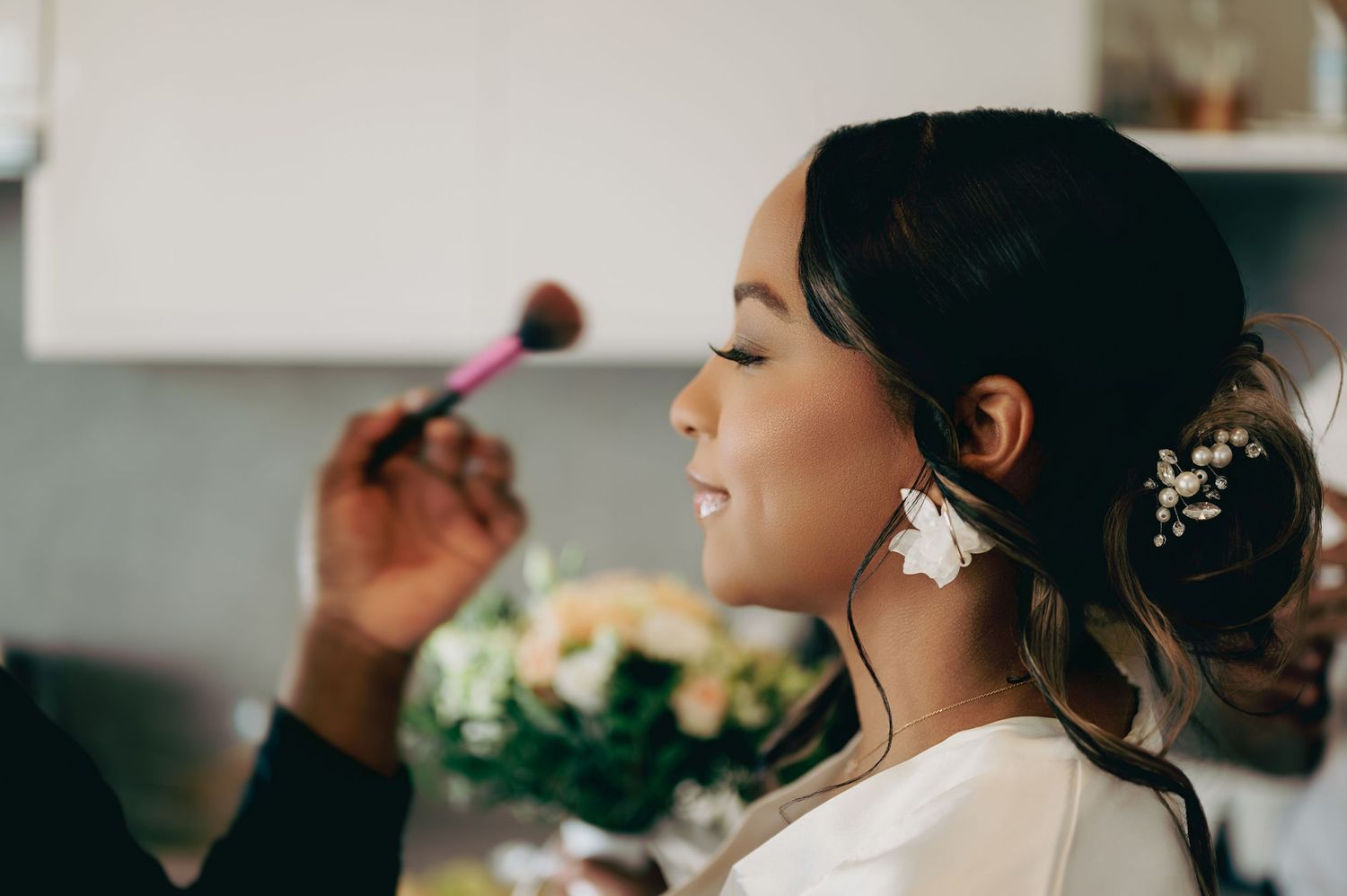 Bride getting makeup done with floral hair accessory and white robe on.