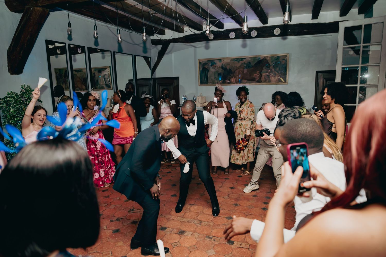 Energetic wedding reception dance floor with guests celebrating and groom dancing at center.