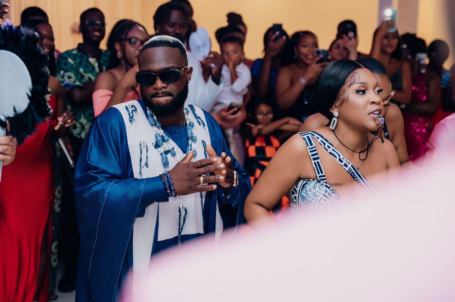 Wedding guests in colorful attire clapping and celebrating at a lively reception party.
