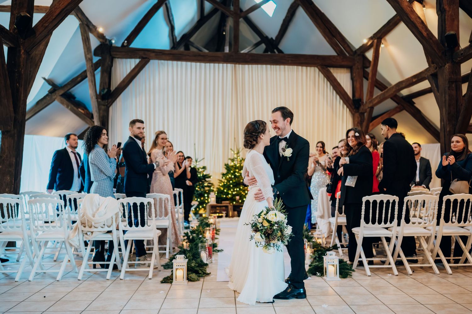 Newlyweds share first kiss at altar in rustic barn decorated with white chairs.