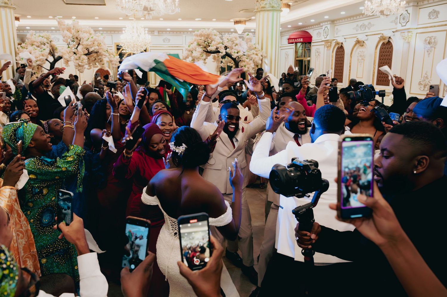 Lively wedding reception celebration with guests dancing, cheering, and recording on smartphones.