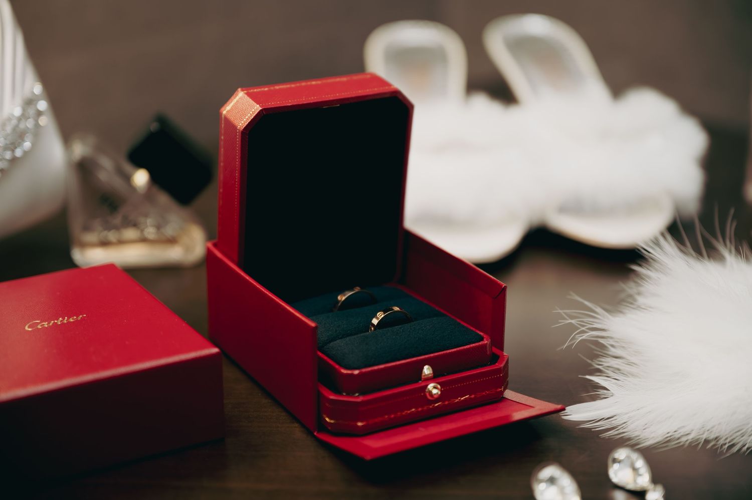 Two gold wedding bands displayed in a red Cartier jewelry box with bridal accessories nearby.