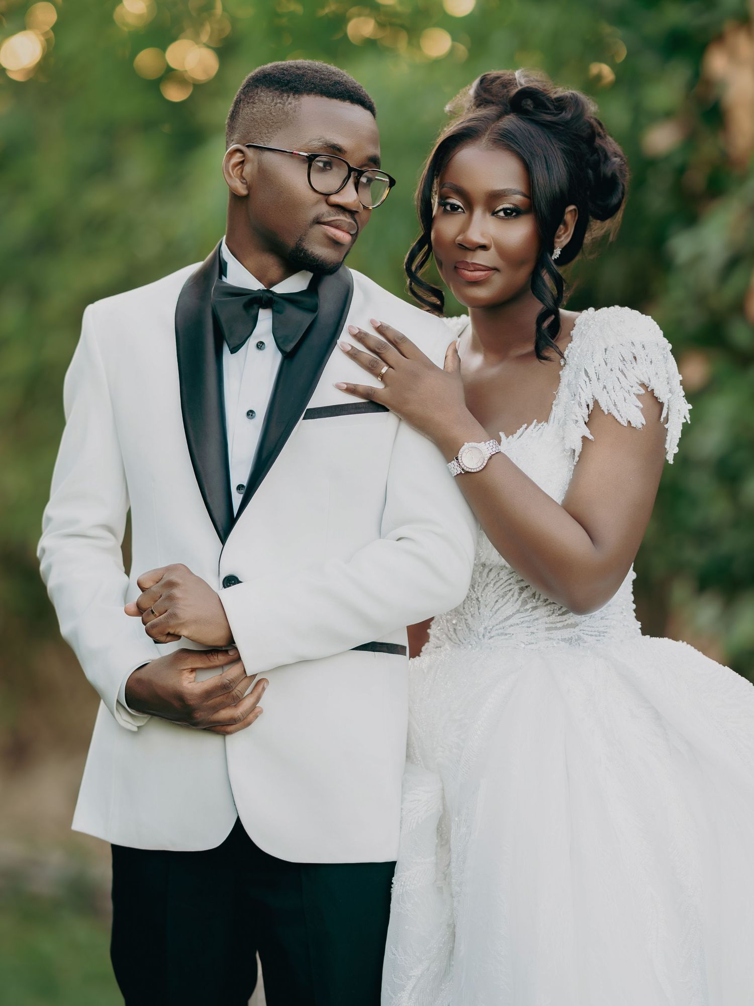 Elegant couple poses together, groom in white tuxedo and bride in lace wedding gown.