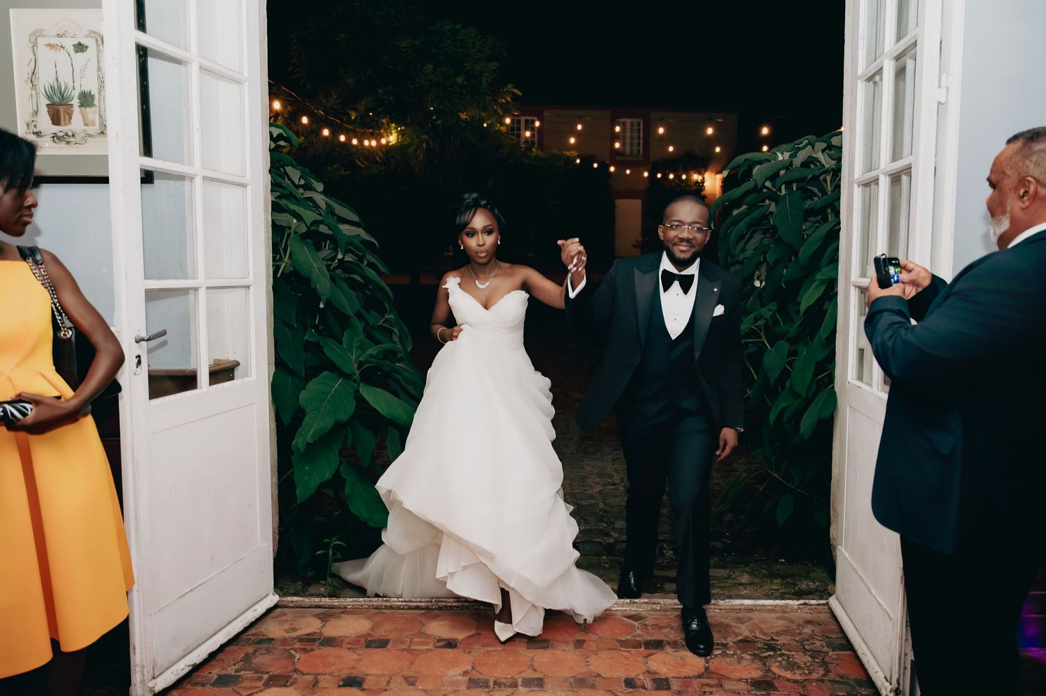 Bride and groom make grand entrance through white French doors at elegant evening wedding reception.