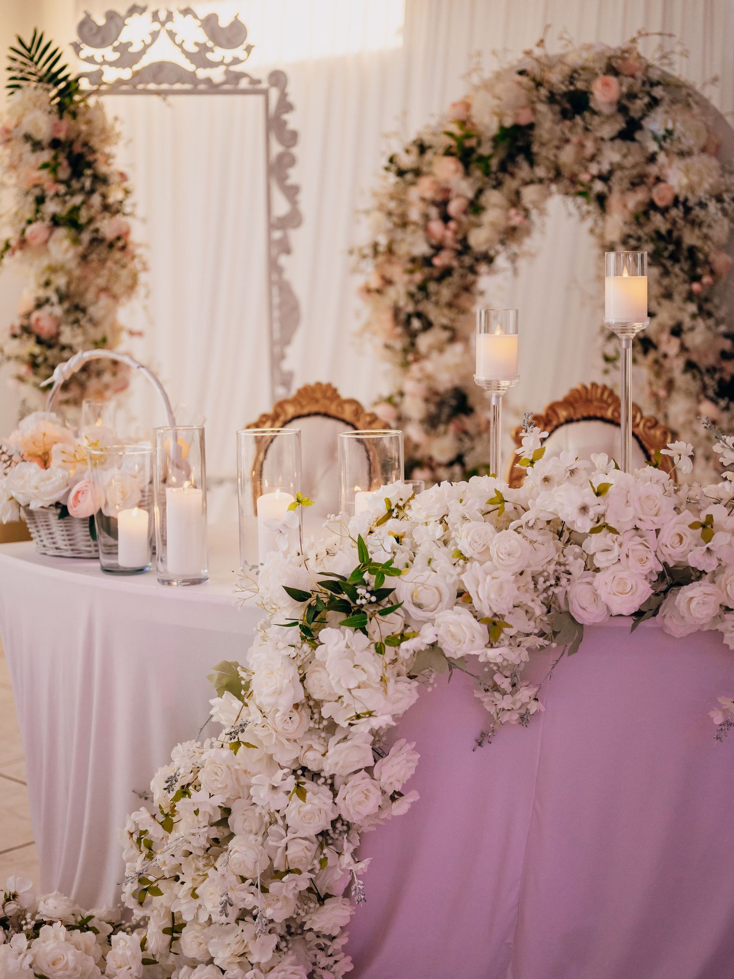 Romantic wedding head table decorated with white roses, candles, and a stunning pink floral arch centerpiece.