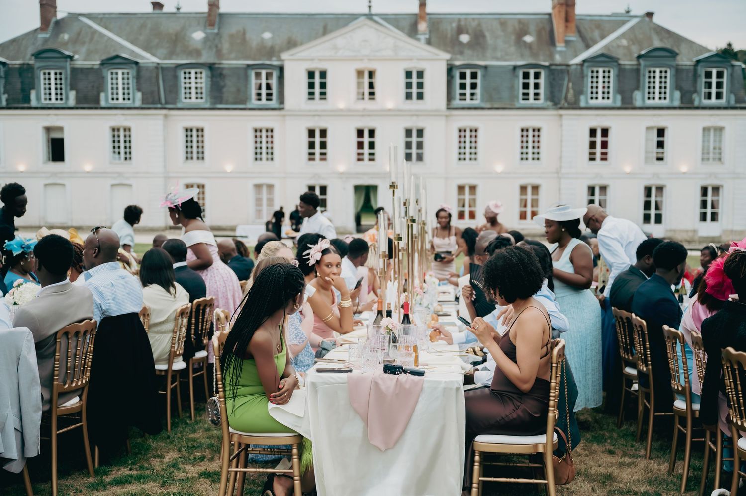 Aerial view of outdoor wedding reception dinner with long tables set before grand French chateau.