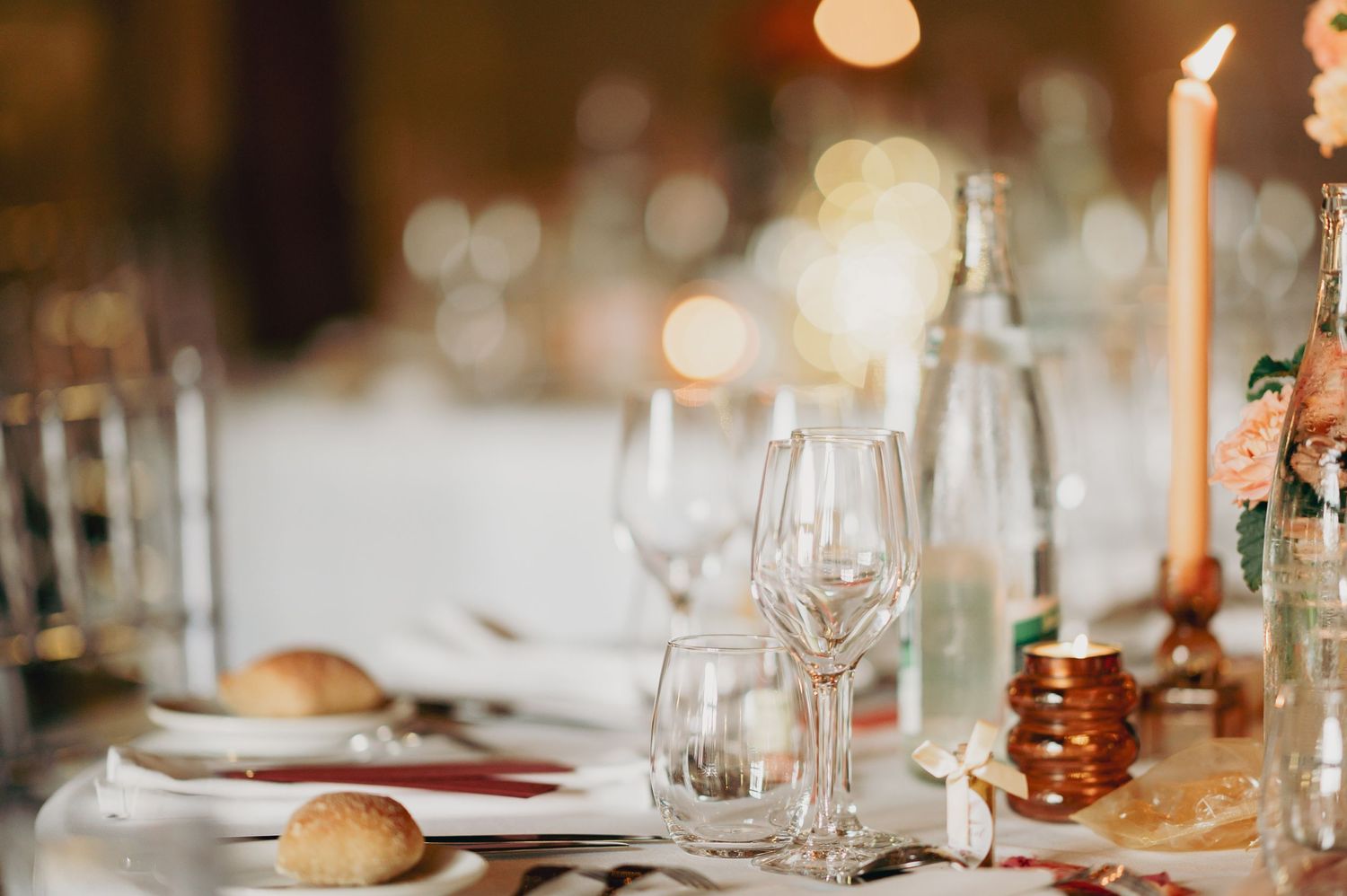 Elegant wedding reception table setting with crystal glassware, candles, and soft bokeh lighting.