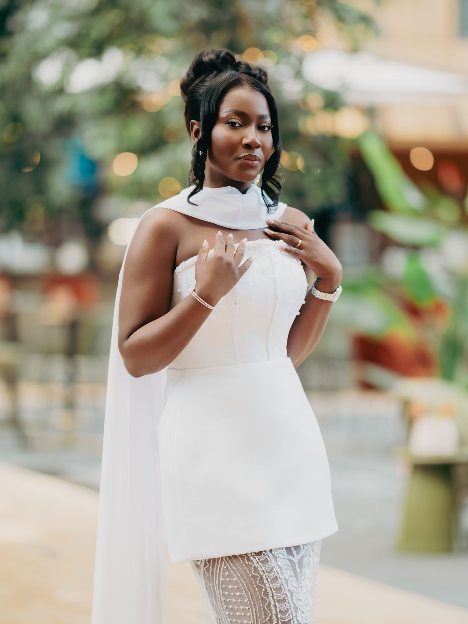 Beautiful bride in a white strapless gown with cape detail posing in a garden setting.