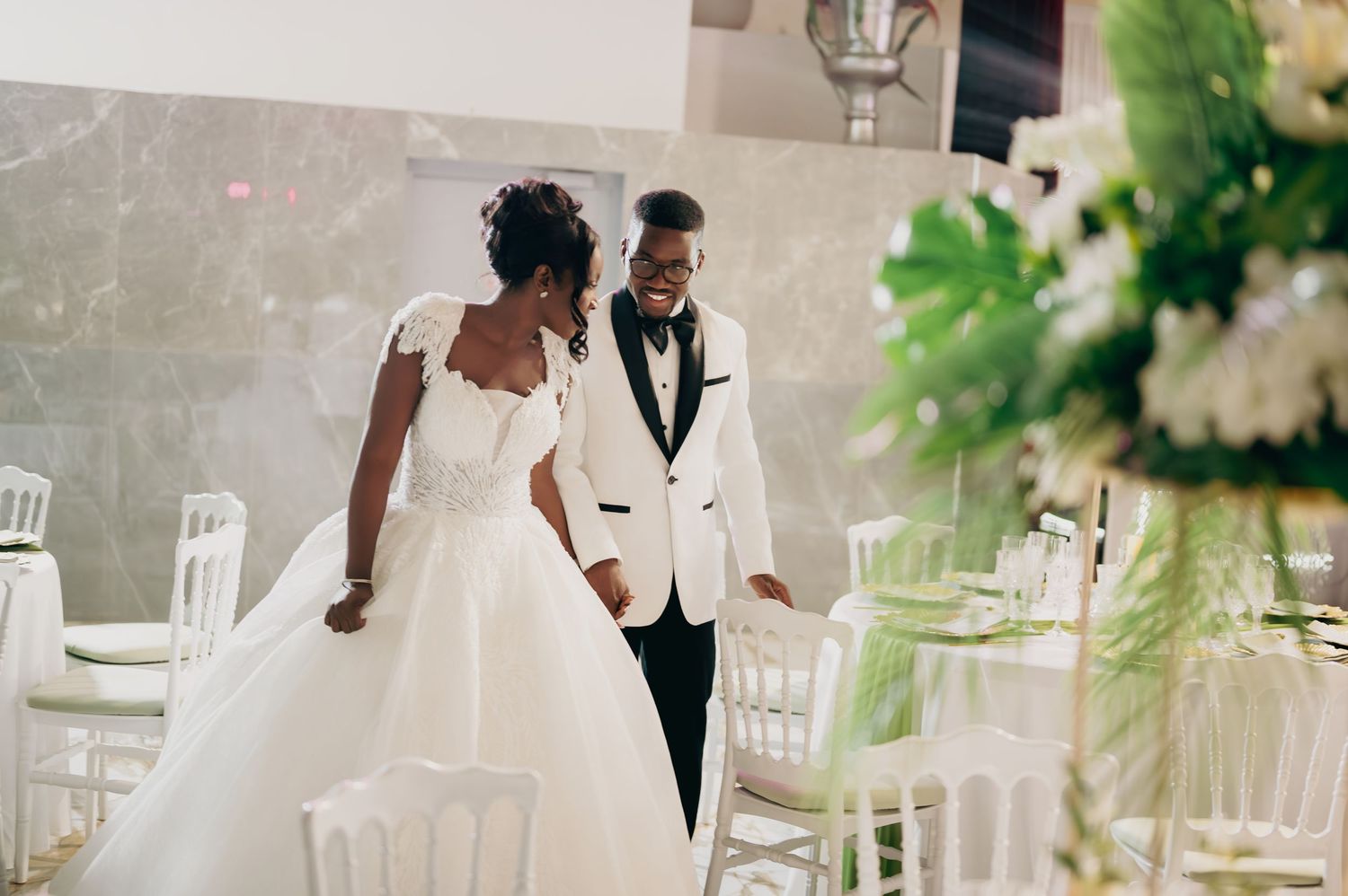 Newlyweds walk hand in hand through beautifully decorated white wedding reception venue.