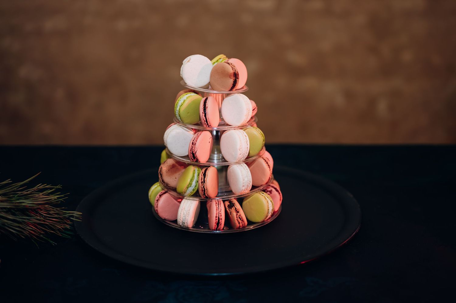 Colorful macaron tower in pink, green, and white arranged on a black plate.