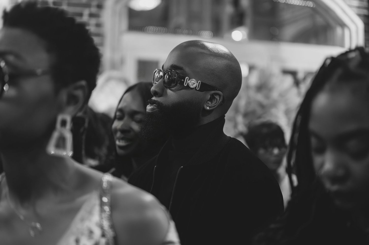 Black and white photo of a bald man laughing joyfully with guests at a wedding celebration.