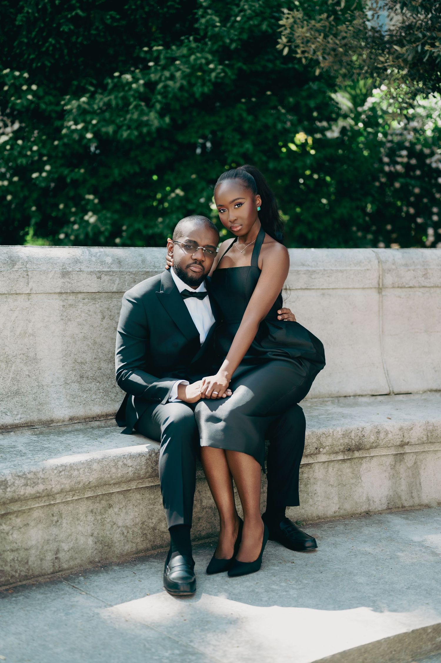 Poised Black couple in matching black formal wear pose together on outdoor stone steps.