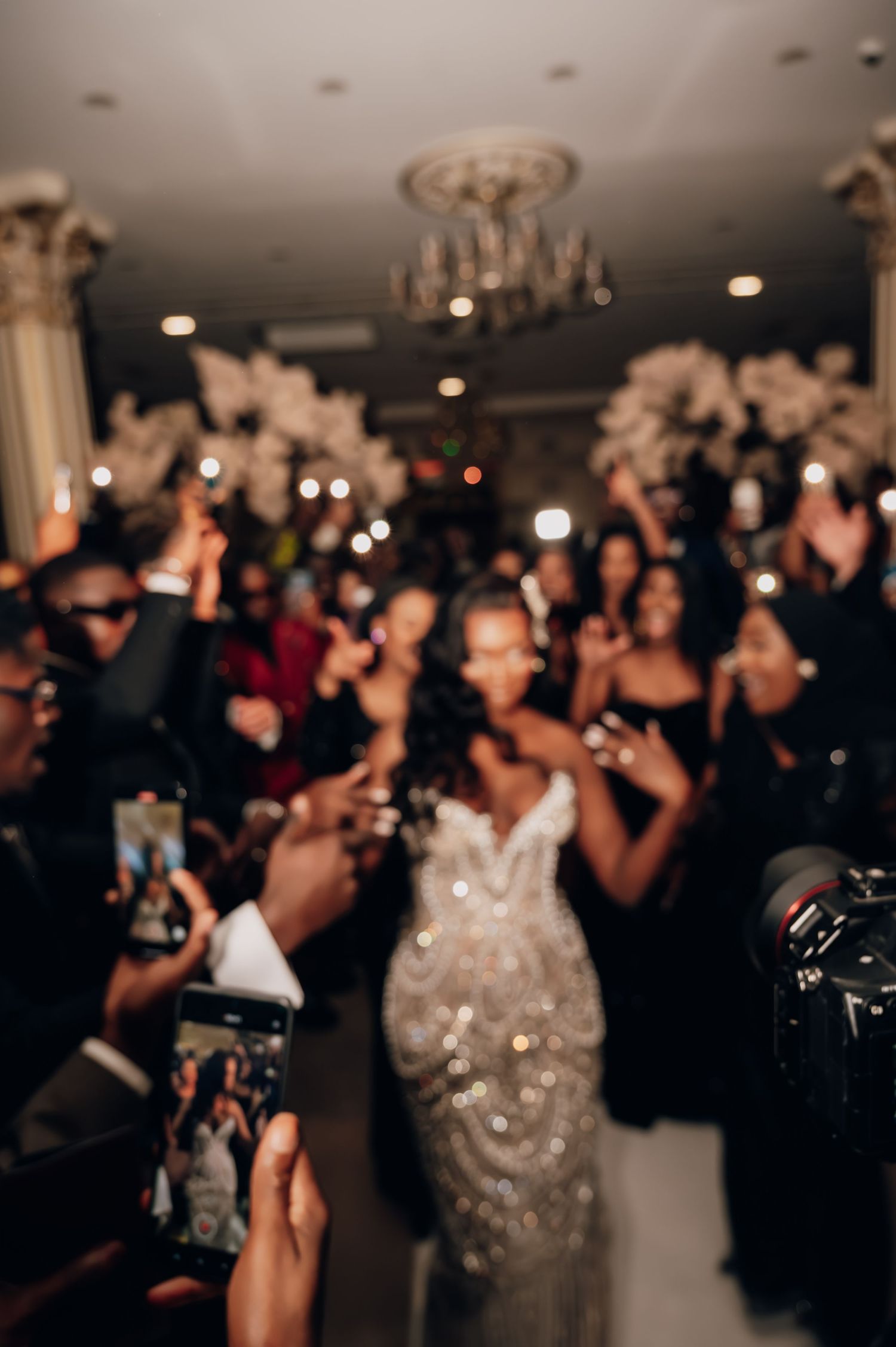 Bride in beaded gown makes grand entrance surrounded by cheering guests.