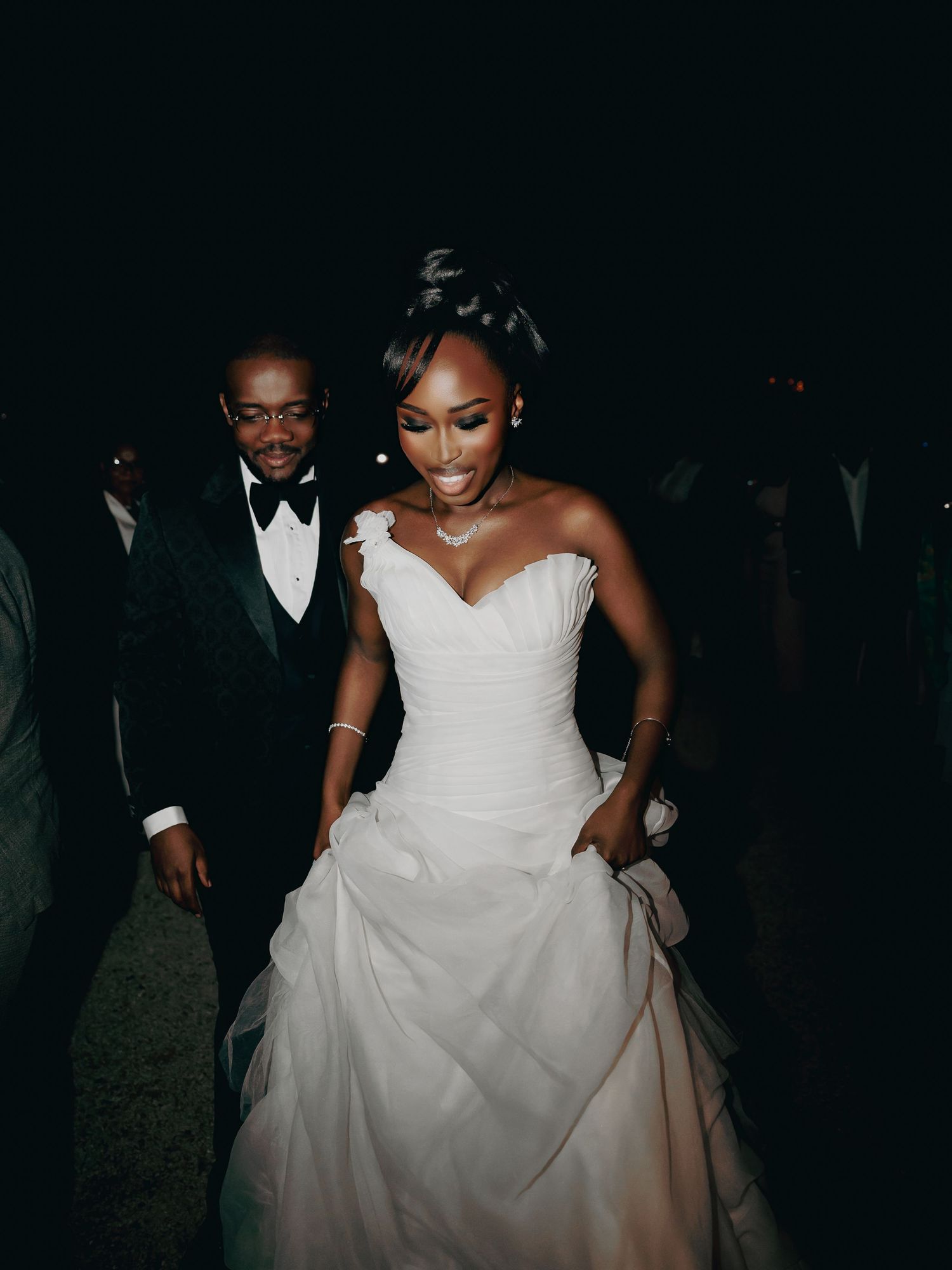 Bride in white ballgown wedding dress smiling with groom in tuxedo during outdoor evening reception.