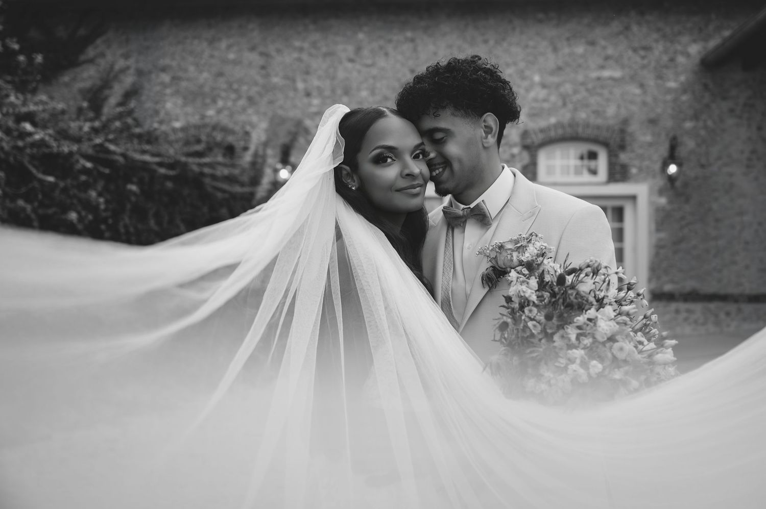 Stunning black and white wedding portrait featuring a couple embracing with an elegant billowing veil.