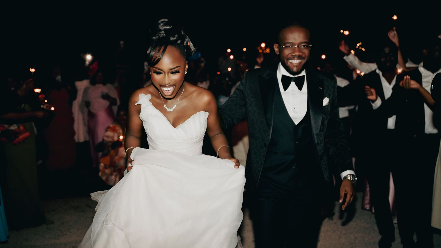 Happy newlyweds walking through a sparkler exit at their nighttime wedding reception celebration.