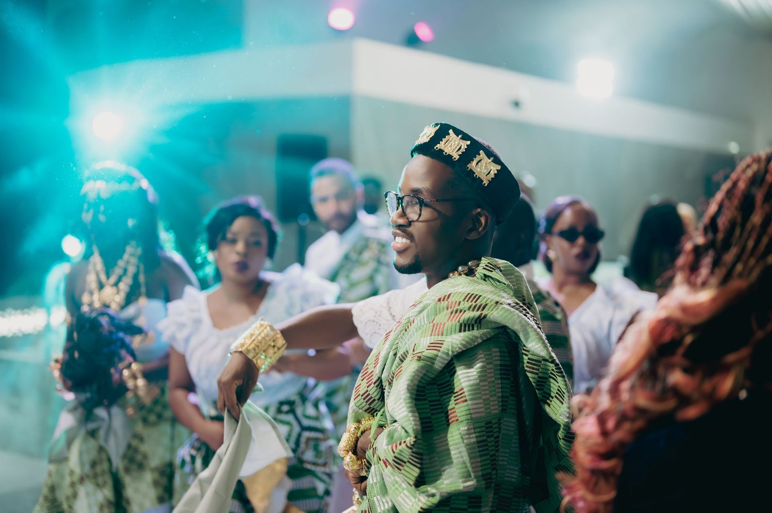 Woman in traditional African attire with gold crown dancing joyfully at a vibrant wedding celebration.
