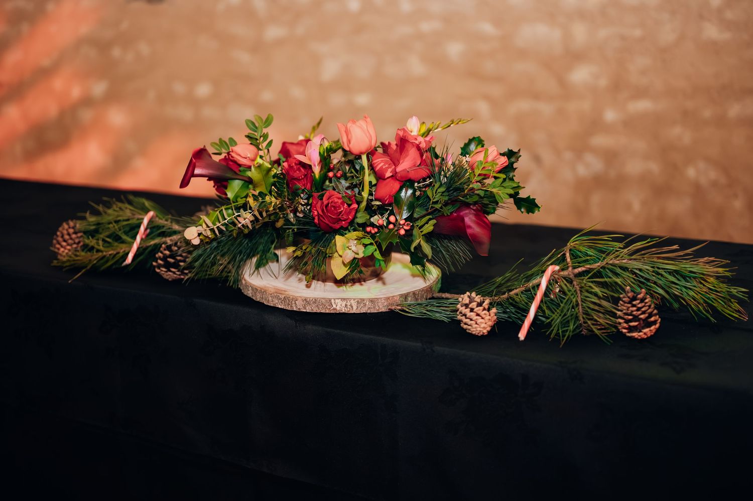 Elegant winter wedding centerpiece with red roses, pine cones, and greenery on black tablecloth.