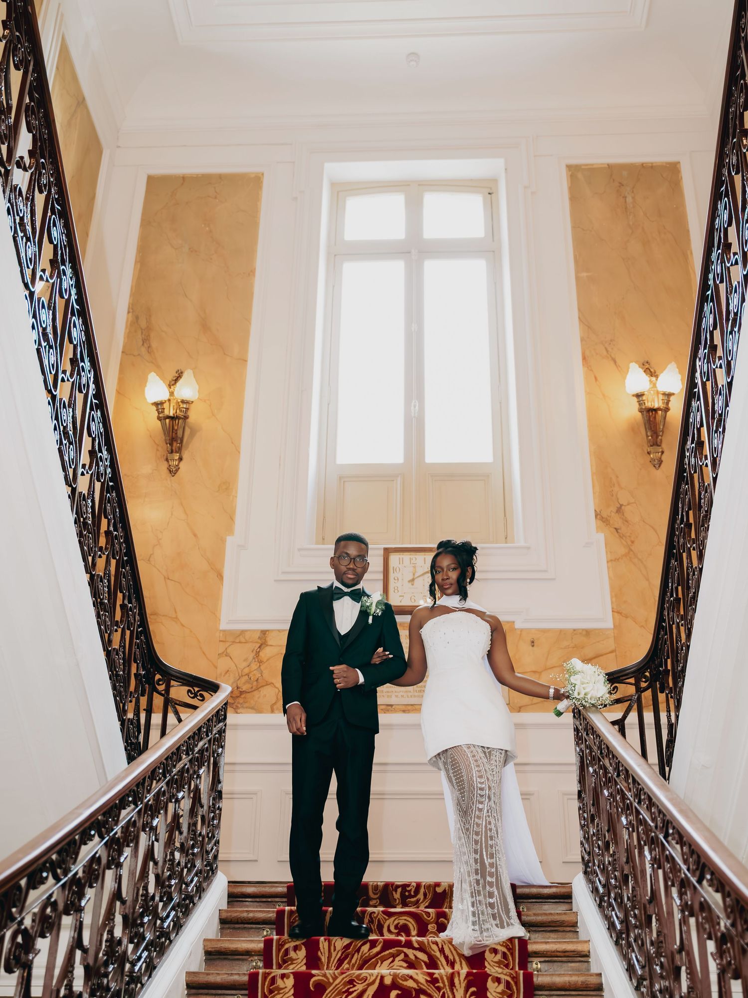 Bride and groom standing together on an elegant grand staircase with ornate iron railings.