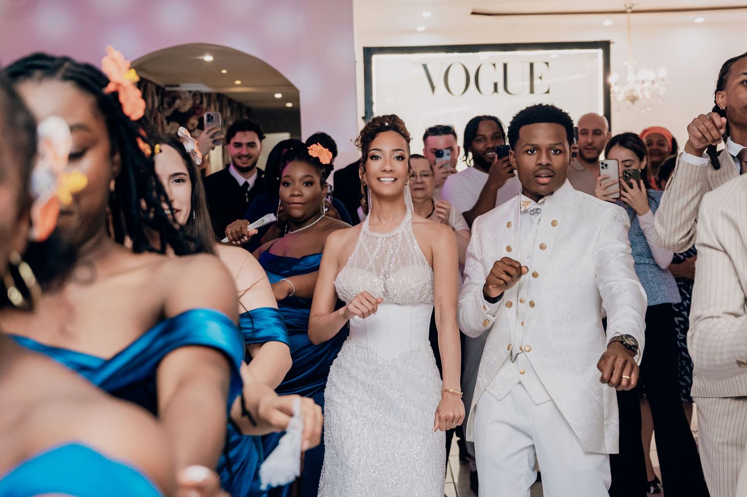 Bride in white feathered gown and groom in white suit entering wedding reception.