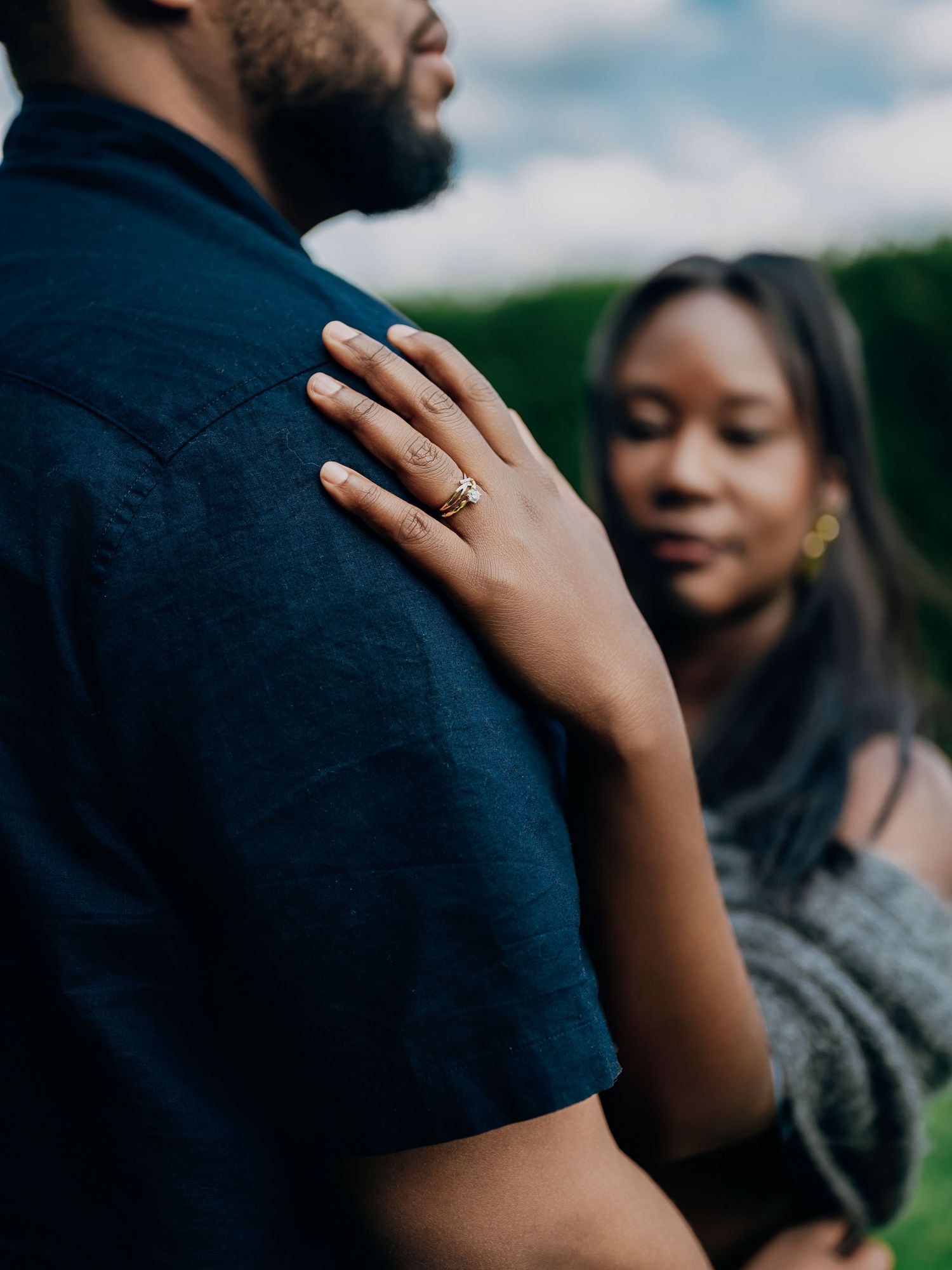 Close-up of woman's hand with diamond engagement ring resting on man's navy blue shirt.