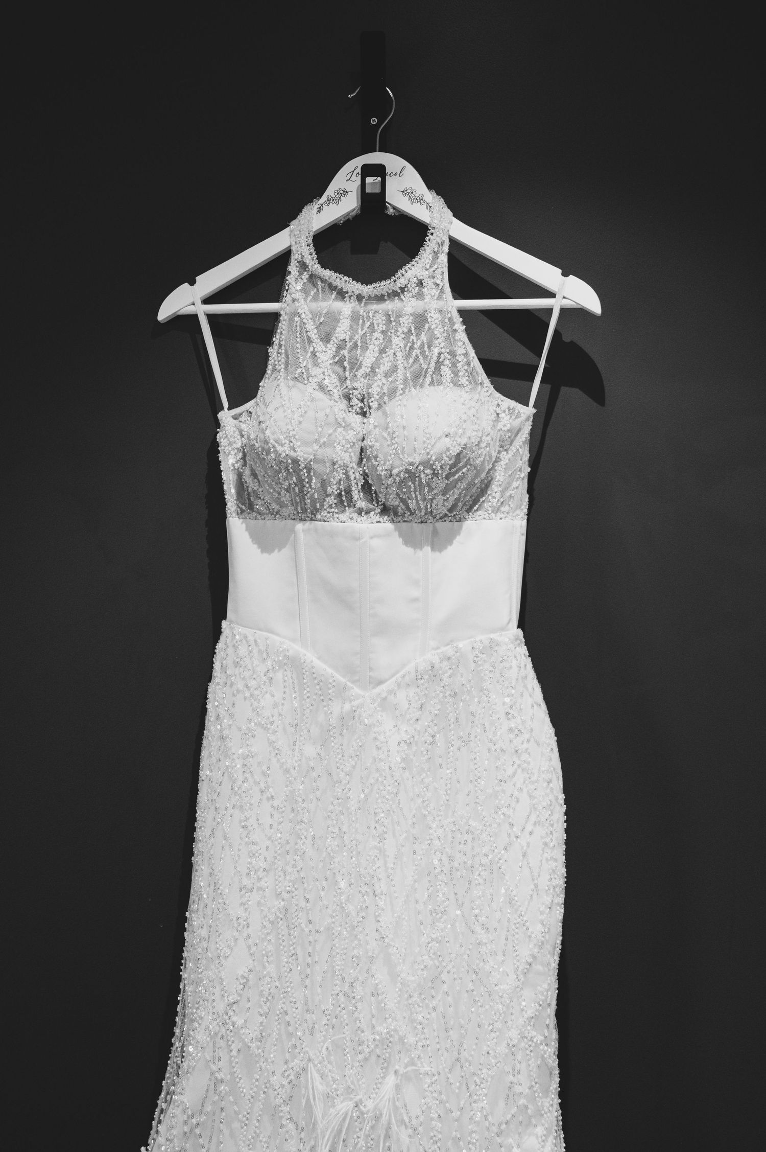 Beaded halter-neck wedding gown with intricate lace detailing hanging on white hanger.
