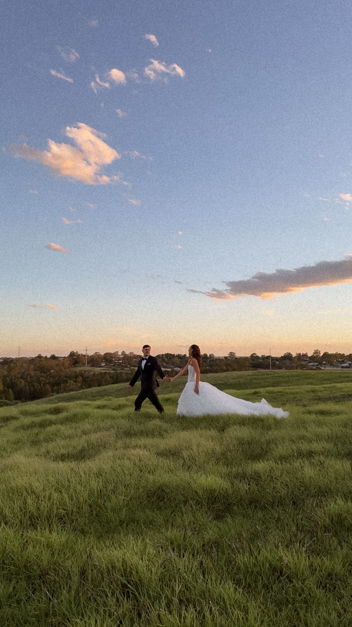 Wedding couple poses dramatically in a green field during sunset.