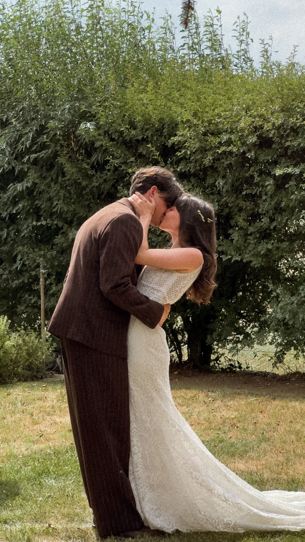 A romantic wedding kiss in a garden setting with green foliage backdrop.