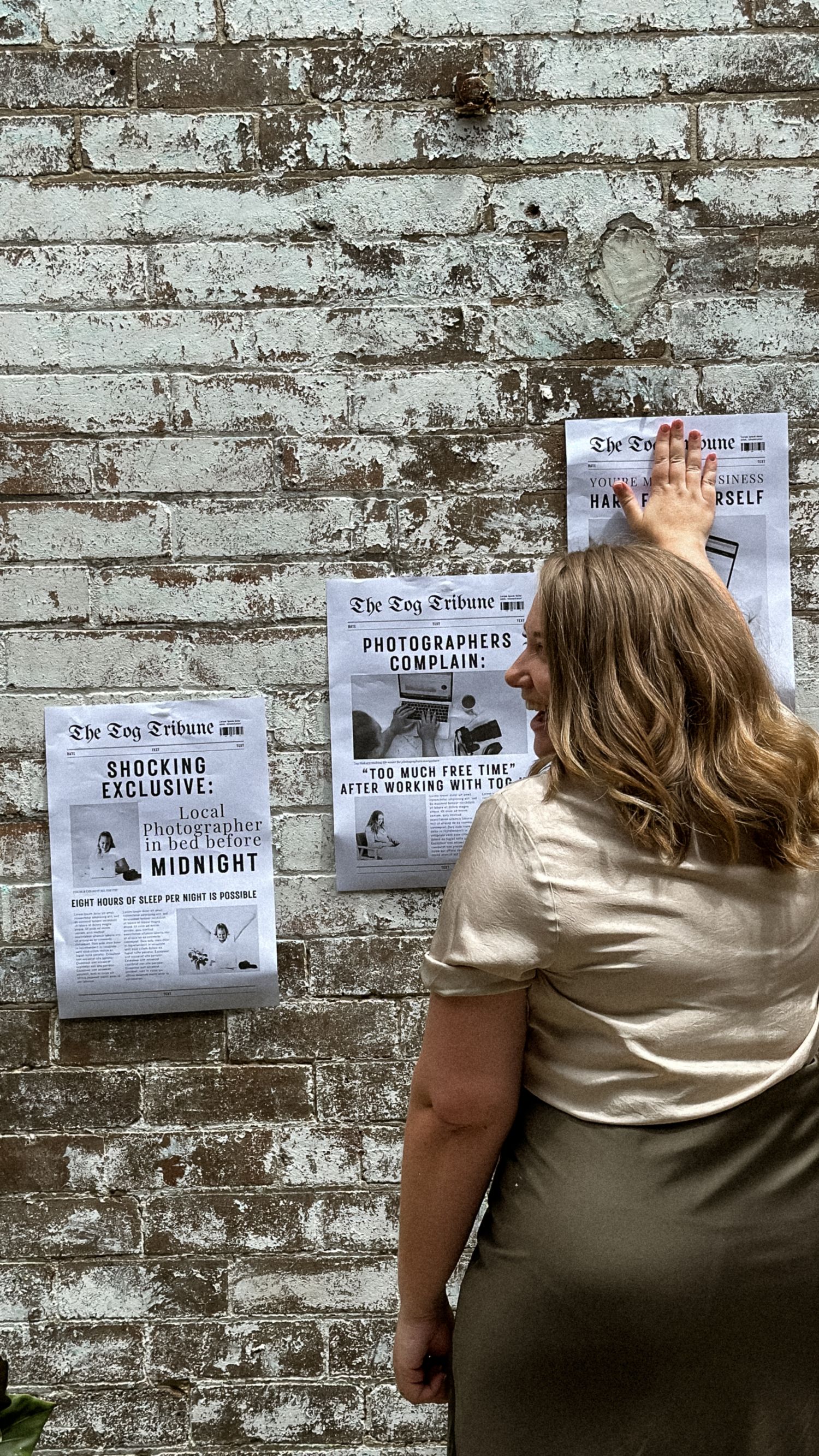 Person in beige clothing posting papers on a weathered brick wall with text visible.