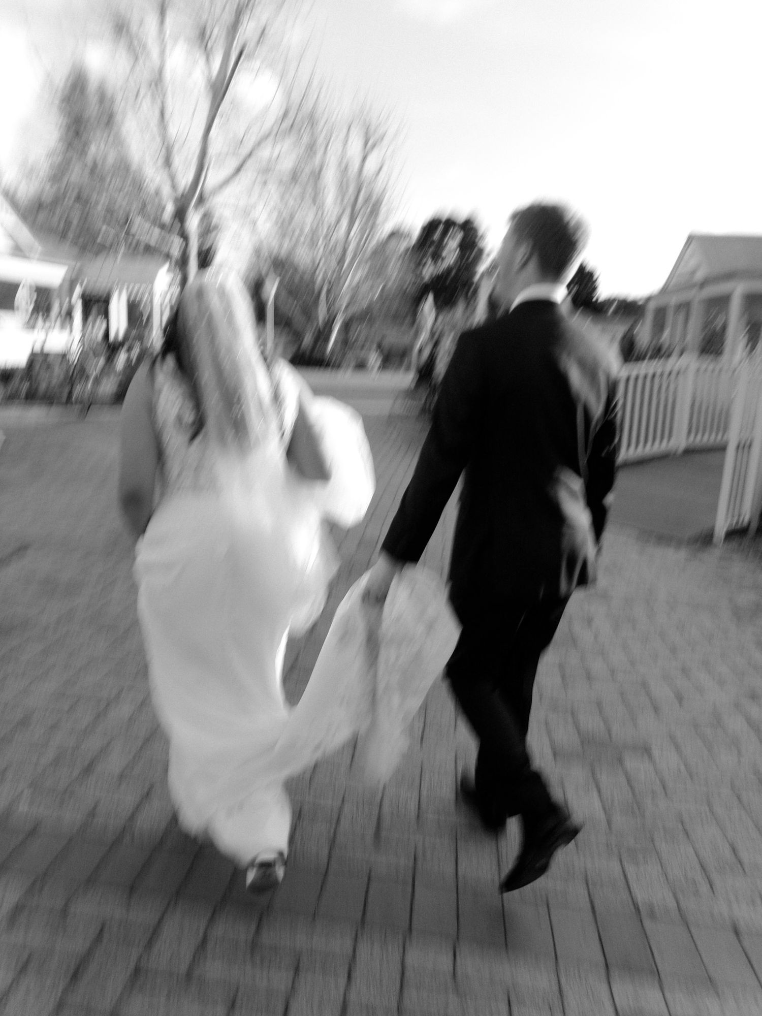 A blurred motion shot of a couple walking on a paved path in wedding attire.