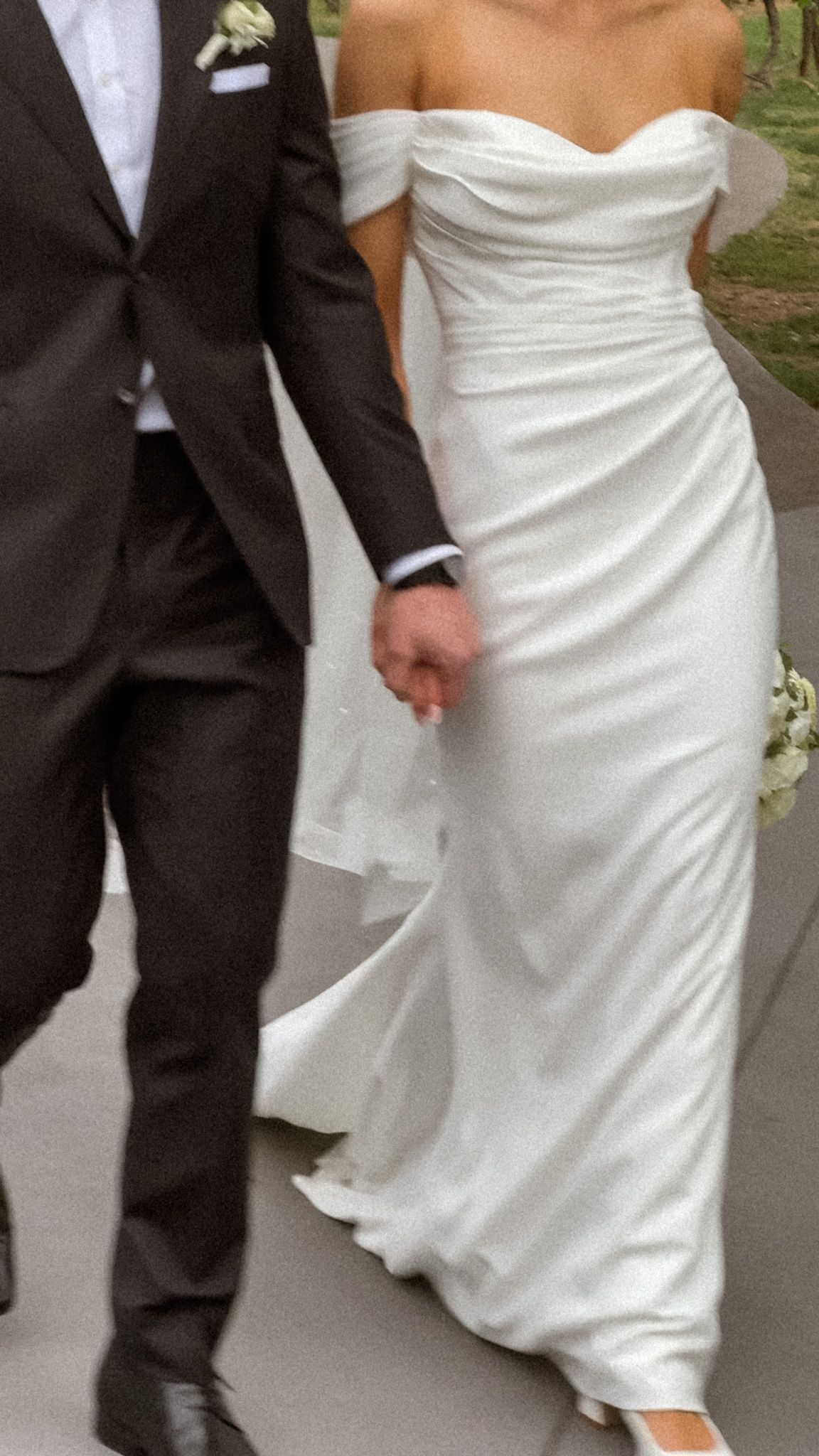 Close-up view of a white wedding dress and black tuxedo as couple walks together.