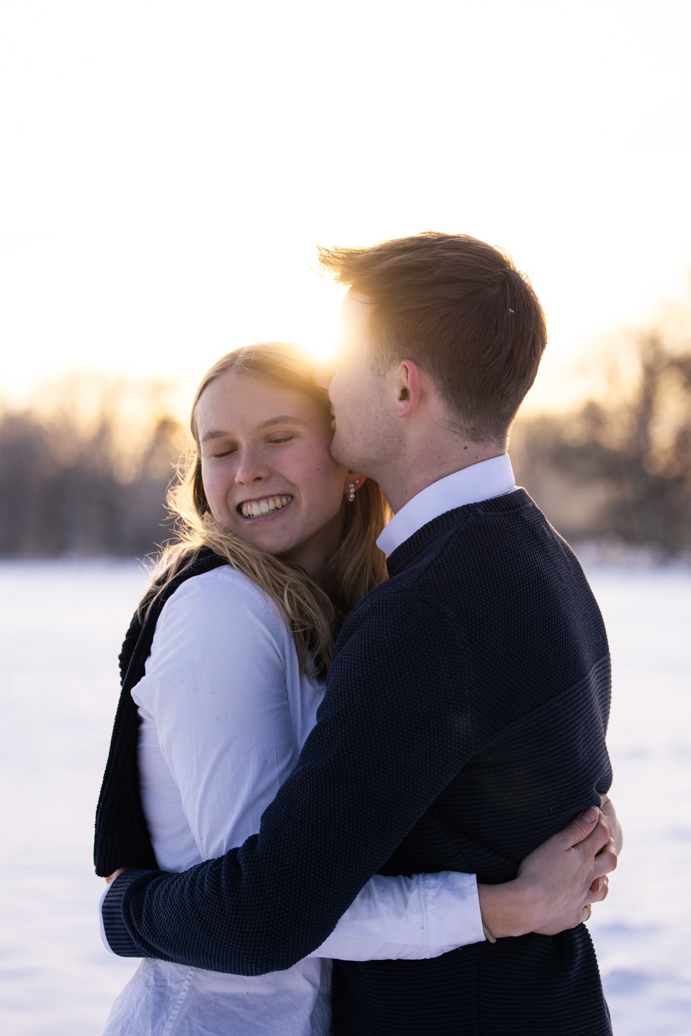 Couple embracing in winter scene with golden sunset light behind them.