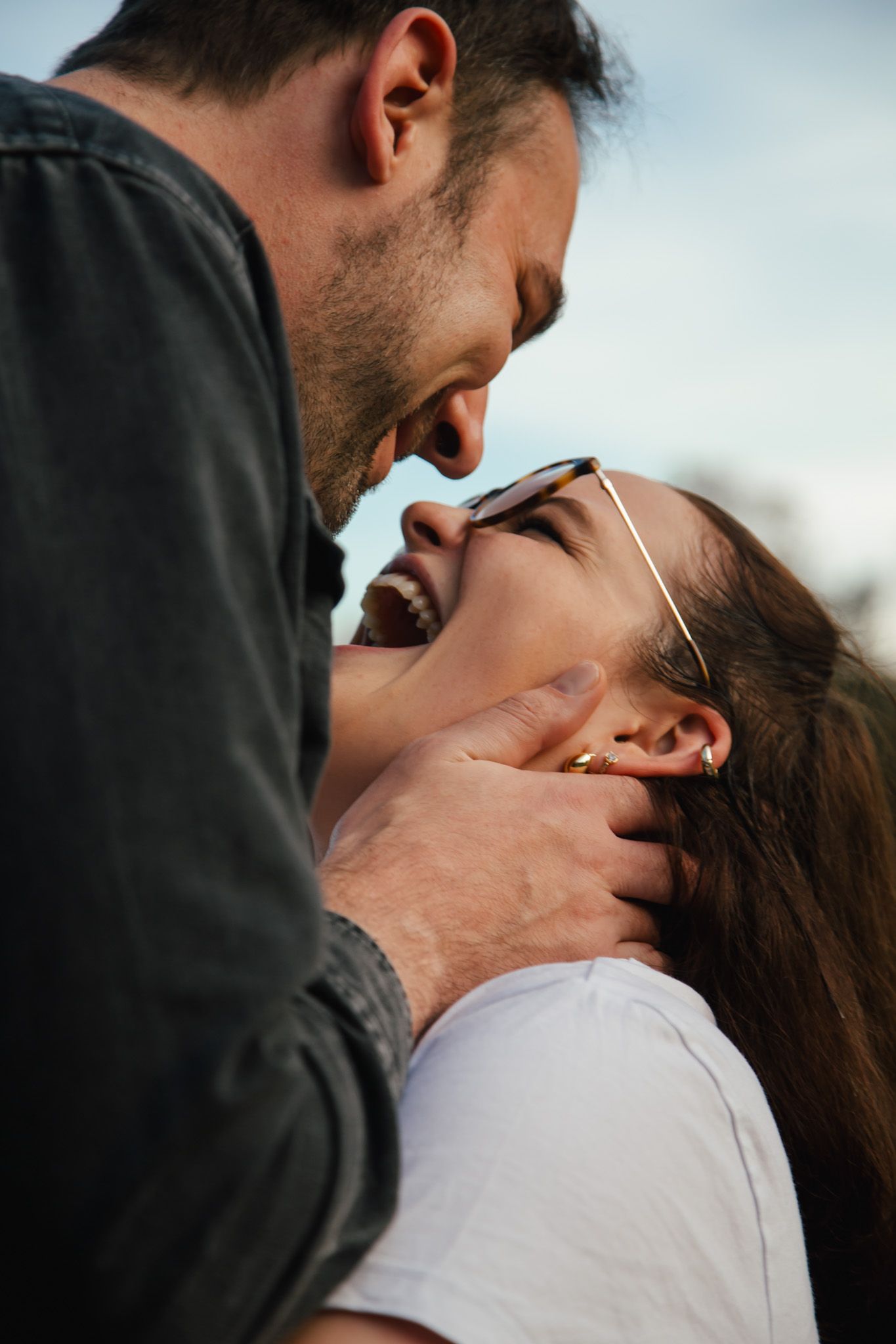 Intimate close-up portrait of couple against soft sky background.