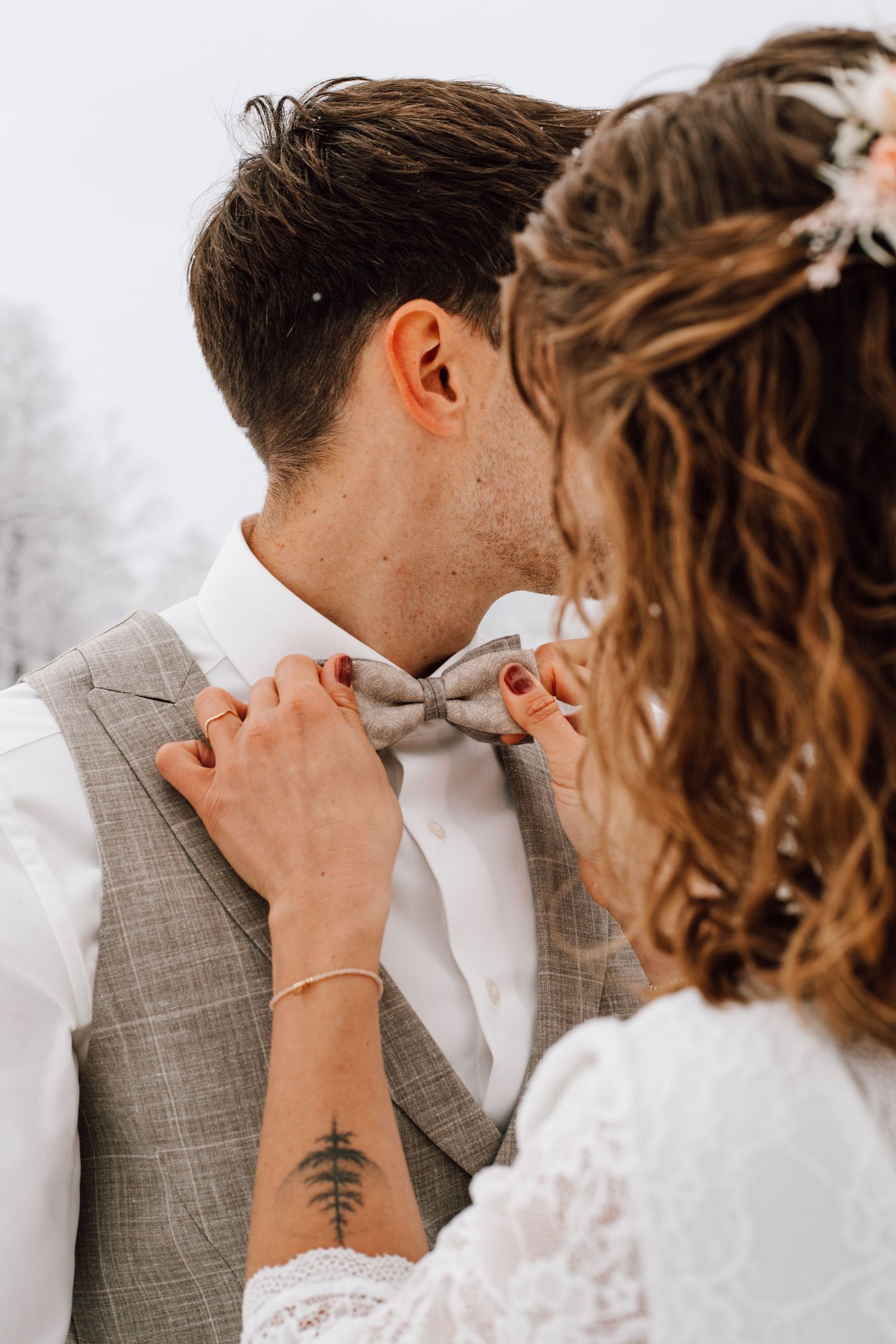 Close-up of hands adjusting grey bowtie on groom's formal attire.