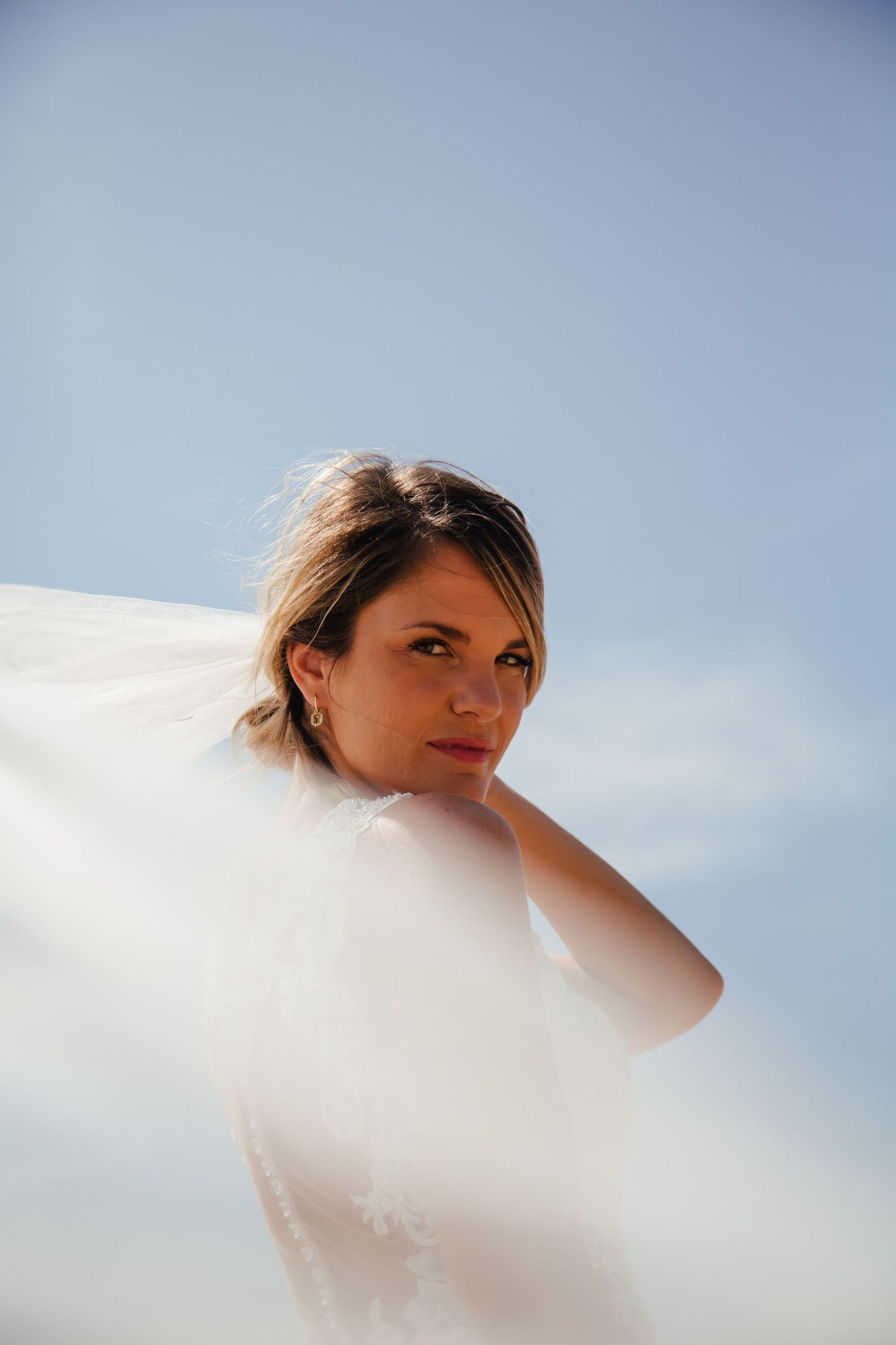 Ethereal bridal portraits against a bright sky with flowing veil movement.