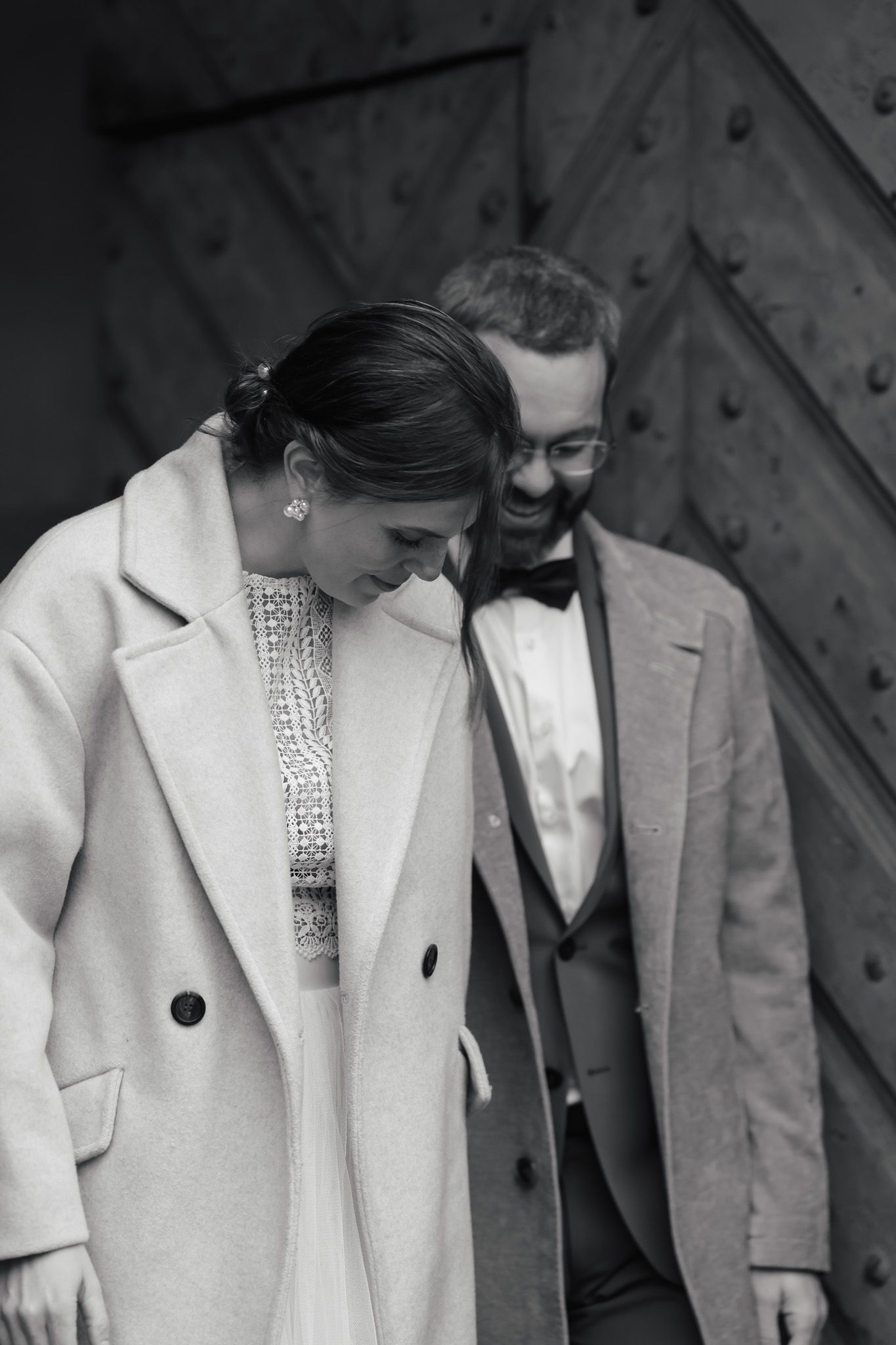 Elegant black and white portrait showing couple in formal attire against textured wall.
