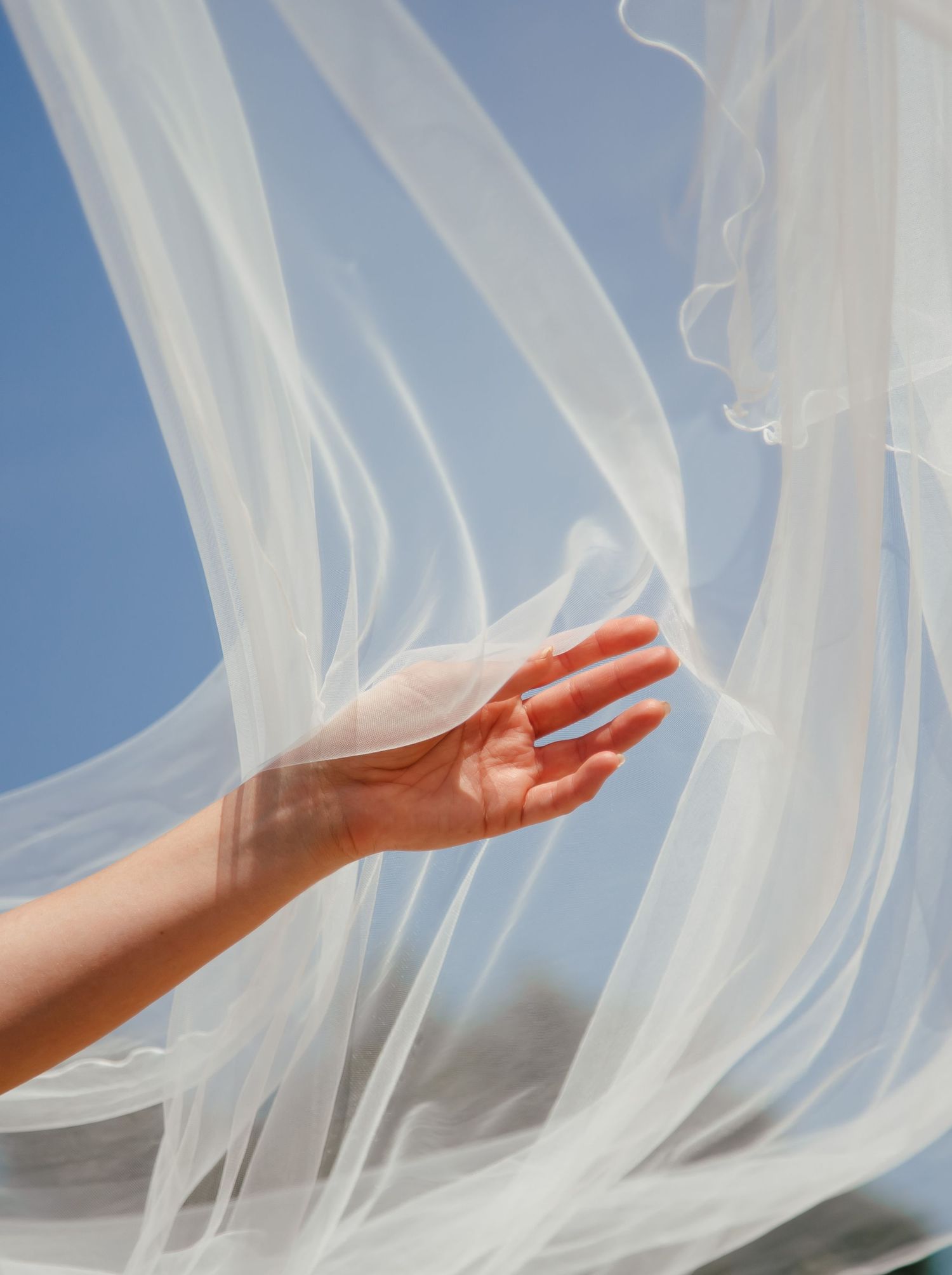 Flowing white sheer fabric billowing in the wind against blue sky.
