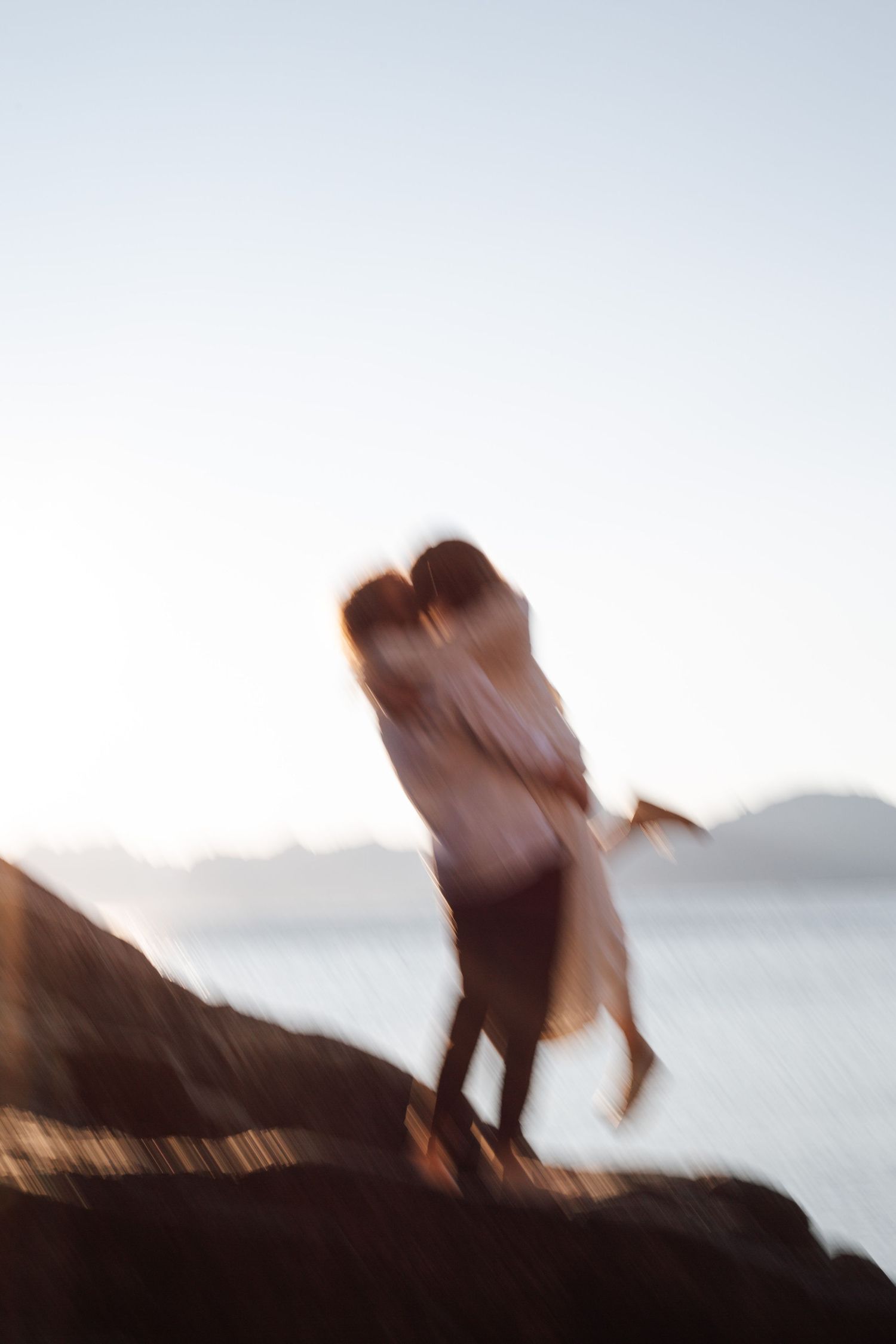 Blurred motion capture of couple embracing on cliff edge at dusk.