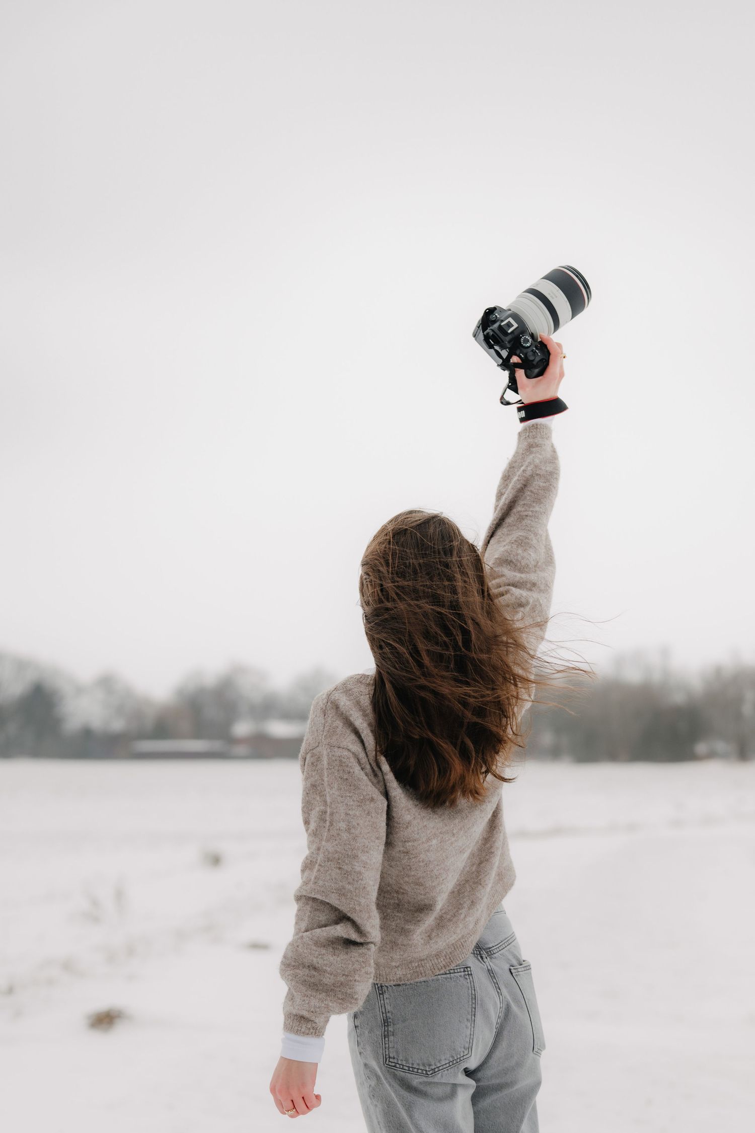 Photographer in winter landscape holding camera with snow-covered ground.