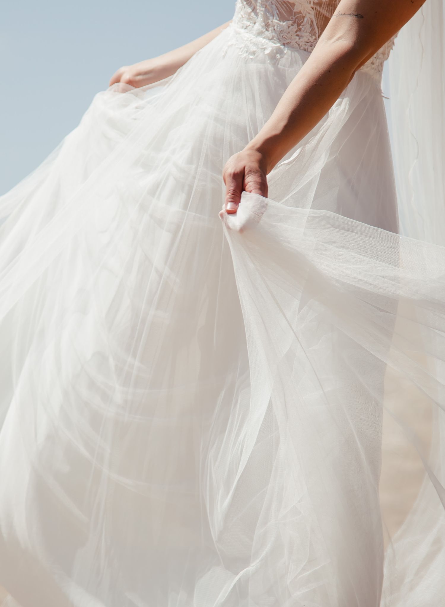 Delicate white tulle fabric of a wedding dress being gently held and arranged.