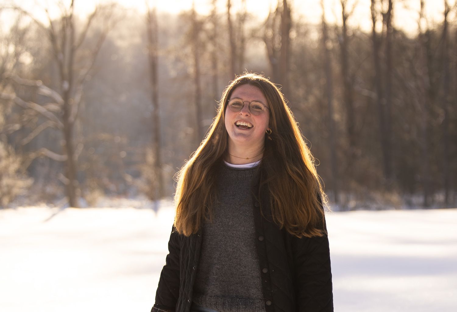 Person laughing joyfully in winter scene with snow-covered trees in background.