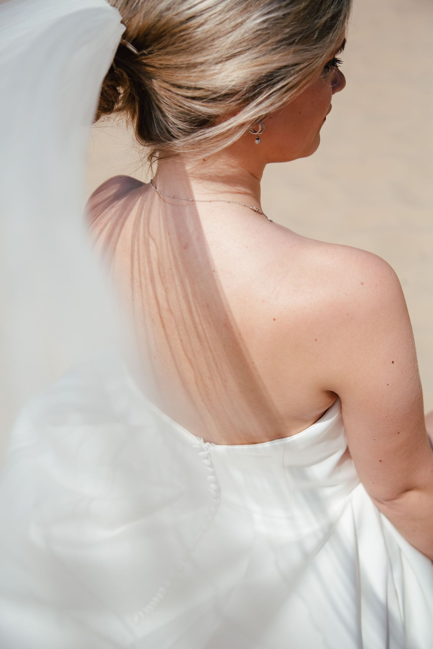 Back view of bride in white dress showing elegant bare shoulders and updo hairstyle.